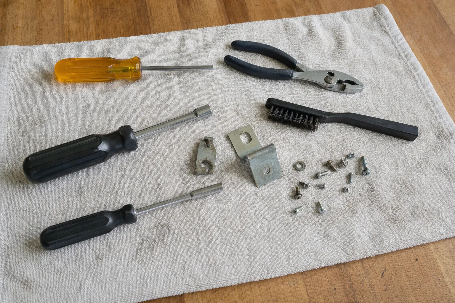 Nut drivers, screwdrivers, pliers and a wire brush laid out on a towel beside brackets and screws